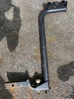 Full view of the black metal bike trailer hitch showing right-angle design, drop hitch, and trailer ball attachment with some surface rust and wear.