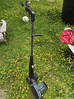 Full view of Black & Decker electric lawn edger standing on grass with yellow flowers.