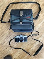 Canon AV-1 camera body and Tokina camera case placed on wooden floor, showing full lot contents.