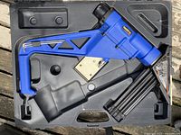 Blue FastenMaster FloorNailer flooring tool positioned in molded black plastic carrying case on wooden surface.
