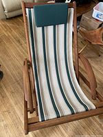 Close-up front view of the wooden lounge chair showing striped fabric and green headrest, set on a hardwood floor.