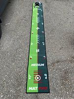 Full view of the rectangular golf training mat showing measurement markings in feet and arrows for alignment, green surface with white and red markings, labeled 'MEDIUM MAT PRO'.