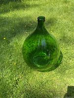 Green glass container placed upright on grass, showing the rounded bulbous shape and narrow neck.