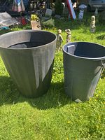 Photo showing the large black plastic planter pot beside a regular garbage can for size comparison, revealing its tall and wide size.