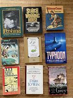 Nine assorted books arranged in a 3x3 grid on a wooden floor. Covers visible showing titles and author names.