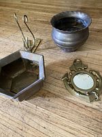Top view of four brass items on wooden surface: anchor mirror, hexagonal planter, brass wall hook, rounded brass pot