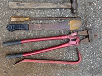 Photo showing six assorted hand tools laid on the ground: hammer, screwdriver, machete, bolt cutters, crowbar, and pipe wrench.