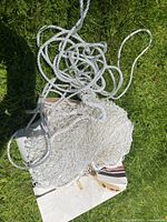 Photo showing folded white rope net lying on grass, coiled and neatly arranged to show its rope material and knots.
