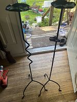 Pair of tall black metal candle holders standing on wood floor in a doorway, showing full height and base design.