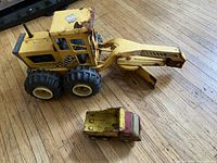 Photo of two Tonka construction toys on wooden floor, showing large yellow loader and smaller dump truck.