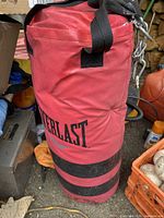 Red Everlast punching bag with black straps and chain for hanging, placed on ground, visible branding and wear.