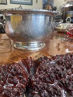 Side view of silver plated bowl showing embossed decorative pattern and two handles, placed on wood surface.