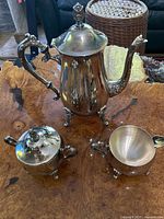 Top view of the silver plated teapot with sugar bowl and creamer on a wooden table.
