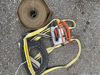 View of two nylon slings and an electric jigsaw on pavement.