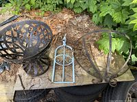 Set of three wrought iron garden items on the ground surrounded by leaves and plants