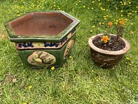 Two ceramic garden pots placed on grass: one large hexagonal green glazed pot with decorative motifs and one smaller round brown pot with plants inside.