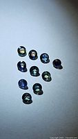Photo of ten small round cut bi-colored sapphires showing deep blue and yellow hues on a blue-gray surface.