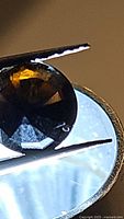 Close-up photo of a deep dark cognac yellow round cut tourmaline gemstone held by tweezers showing faceted surfaces and rich color.