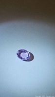 Oval cabochon purple amethyst gemstone placed on white surface showing polished domed top and transparent purple color.