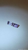 Photo of two emerald cut amethyst gemstones laying side by side showing the size and color