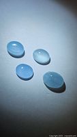 Four natural strong blue aquamarine oval cabochon gemstones on white background with spotlight illumination.