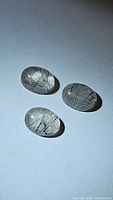 Close-up photo of three oval cabochon-shaped black rutilated quartz gemstones showing needle-like black inclusions inside transparent quartz.