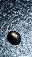 Natural black star sapphire oval cabochon on textured dark background showing some reflection and partial star effect.