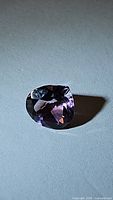 Faceted pear-shaped natural amethyst gemstone placed on a flat surface, showing color and clarity in natural light.