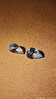Two pear-shaped aquamarine gemstones placed on a brown textured surface.