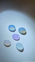 Five oval mixed color chalcedony cabochon gemstones on white background with diffuse light, showing color variation and translucency.