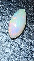 Close up photo of the natural Ethiopian opal marquis cabochon gemstone displaying vivid rainbow flashes and full fire on a black textured background.