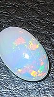 Close-up photo of natural Ethiopian opal oval cabochon showing bright multicolor play of color on black textured background.