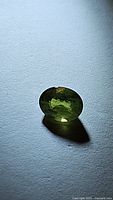 Oval cut natural green sapphire gemstone on a white background, showing reflections and internal characteristics.