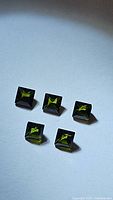 Five natural green tourmaline gemstones arranged on a light background, showing princess cut facets and deep green color.