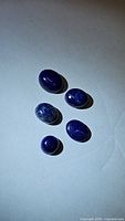 Five polished Lapis Lazuli cabochons in various oval and round shapes on white background, showing color and surface details.