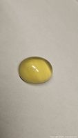 Oval cabochon lemon citrine gemstone on white background, showing polished smooth top surface and lemon yellow color.