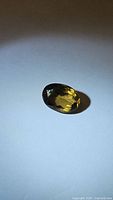 Oval shaped natural Madeira citrine gemstone under direct light highlighting its amber color and faceting.
