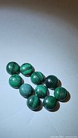 Ten round green malachite cabochon gemstones arranged on white background, showing characteristic banded patterns and polished smooth surfaces.