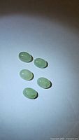 Top view of five small oval cabochon mint green kyanite gemstones on a plain background, showing their translucent color and polished surfaces.