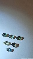 Six natural pear cut sapphires in green and blue hues on a white background, showing size and color variation.