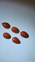 Five natural orange jasper cabochons displayed on a white background showing smooth polished surfaces and mixed oval and pear shapes.