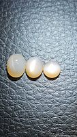 Three natural peach moonstone cabochons placed side by side on textured black background, showing their rolling flash effect.