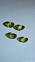 Four natural pear cut apple green peridot gemstones placed on blue background showing clarity and color.