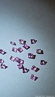 Multiple natural princess cut pink sapphires spread on a surface, showing color and cut.