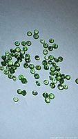 Photo showing scattered small round green tsavorite garnet gemstones polished and faceted on a dark surface.
