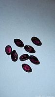 Eight oval cut deep pink-purple rhodolite garnet gemstones laid flat on white background, showing color and shape clearly.