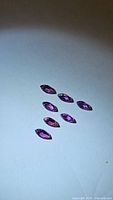 Seven bright pink-purple marquis cut Rhodolite garnet gemstones spread on white background.