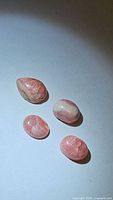 Four natural rhodochrosite stones arranged on white background, showing color and shapes