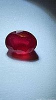 Close-up photo of the oval cut red ruby gemstone showing its shape and some faceting.