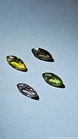 Four natural marquis cut sapphires with different colors: yellow, purple, green, and clear, placed on a white surface under light showing facets and color detail.